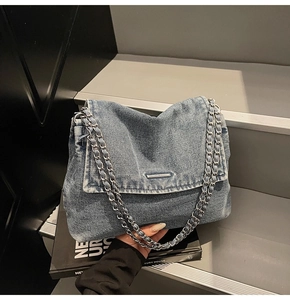 Close-up of blue denim shoulder bag with silver chain strap and metal buckle detail