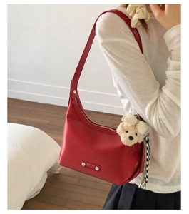 Detail of red leather hobo bag featuring a wide shoulder strap and a cute plush bear charm