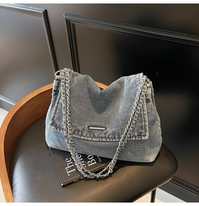 Detail view of washed denim crossbody bag featuring silver metal bar and chain strap