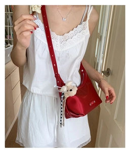 Détail d'un sac à bandoulière rouge brillant avec bandoulière réglable et breloque ours