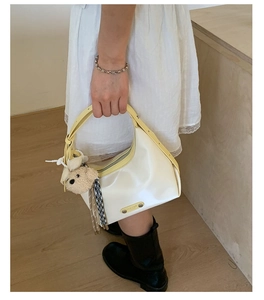 Minimalist creamy white leather shoulder bag with yellow handle and bear charm detail