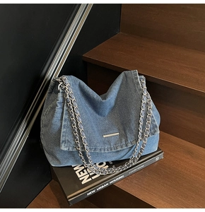 Detail of blue denim shoulder bag showing metallic chain straps on a wooden surface