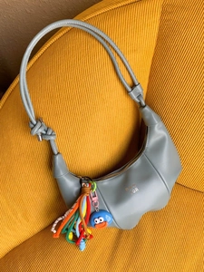 Minimalist grey half-moon bag with gold logo, pleated design and colorful tassel charm