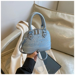 Détail d'un sac coquillage bleu clair orné de strass brillants et zips argentés