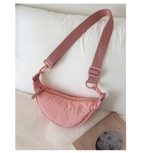 Vue détaillée du sac croissant en nylon rose avec bandoulière large sur un lit doux