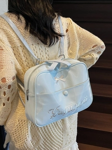 Light blue bow backpack in glossy finish with embroidery worn by a model on stairs