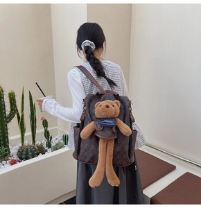 Deep brown printed backpack with a large plush bear charm on a female model back
