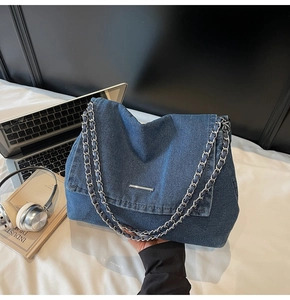 Detail of dark blue denim shoulder bag with silver chain strap and metal bar accent