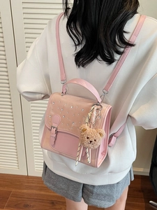 Pink rhinestone backpack with bear keychain shown on model in cozy home setting