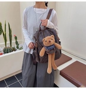 Close-up of printed brown backpack with teddy bear pattern and plush bear charm accessory