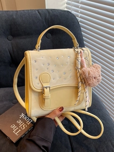 Fashionable light yellow PU handbag with rhinestone decor and bear charm on a grey sofa