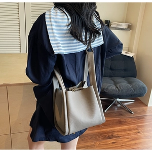 Detail view of the pebbled leather texture and metal feet of this greyish beige bucket bag