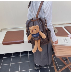 Detail of a brown leather backpack with bear prints and a 3D plush bear on the back
