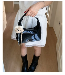 Detail of black patent leather crescent shoulder bag with cute plush bear keychain