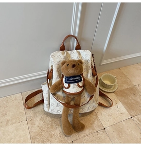 Close-up of a white cartoon pattern backpack featuring a cute brown bear plush pendant