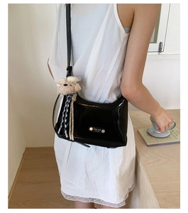 Détail du sac à main noir brillant avec logo en métal et breloque chiot en peluche