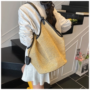 Grand sac fourre-tout tressé avec bordure noire et breloque cœur porté par un mannequin