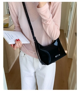 Gros plan d'un sac hobo en cuir verni noir brillant avec un petit logo en métal argenté