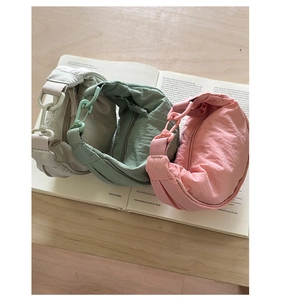 Trois sacs demi-lune en nylon beige, vert et rose sur un livre ouvert