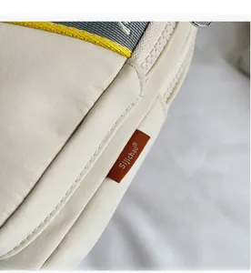 Détail du sac bandoulière avec sangle tissée bicolore et étiquette latérale de marque