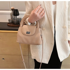 Detail of beige quilted chain handbag with silver buckle held by a model in white blazer