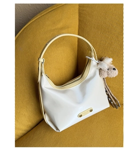 Detail of cream hobo bag with yellow straps and cute teddy bear charm on a sofa