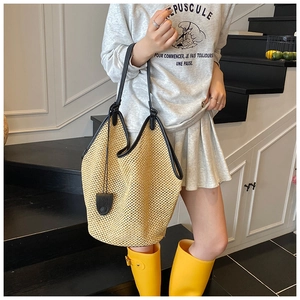 Détail du sac seau en paille beige avec garniture en cuir noir et breloque décorative