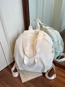 Vielseitiger cremeweißer Nylon-Rucksack mit runder Struktur und Tragegurten auf Holzboden