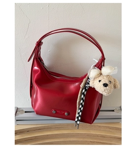 Detail of red leather hobo bag featuring silver zipper and cute plush puppy charm