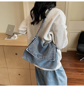 Detail of blue denim shoulder bag featuring metal bar decor and woven chain strap