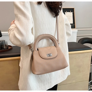 Detail of beige pleated crossbody bag with silver twist lock and round handle worn by model