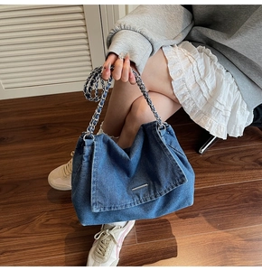 Close-up of denim shoulder bag with silver chain strap and metal bar detail