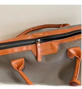Close-up of premium fabric detail with brown leather trim and metallic zipper on travel bag