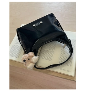 Detail of black glossy patent leather hobo bag with silver logo and plush bear charm