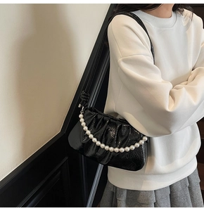 Dettaglio della borsa a nuvola nera pieghettata con finitura lucida e catena di perle