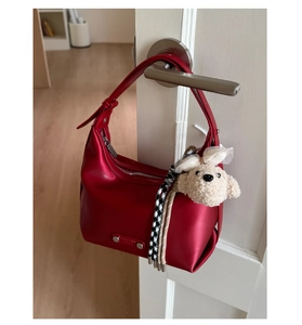Red hobo shoulder bag hanging on a white door handle with plush dog charm and strap