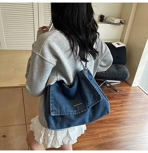 Detail of blue denim shoulder bag featuring metal chain strap and flap stitch texture
