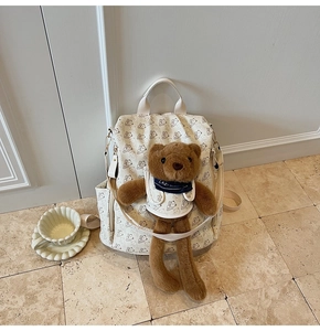 Detail of cream backpack with bear print and cute plush bear charm wearing a blue scarf