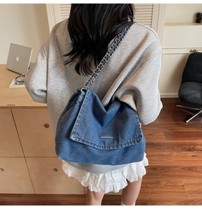 Detailed view of blue denim shoulder bag featuring metal chain strap and flap closure