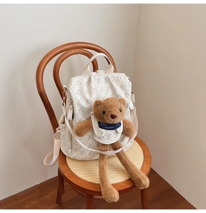 Detail of canvas backpack with bear prints and a plush teddy bear charm on a wooden chair