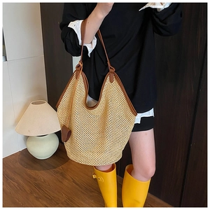 Détail d'un sac cabas en paille tressée avec bordure en cuir brun et pendentif cœur