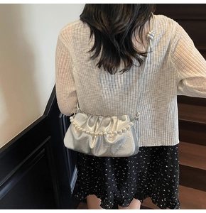 Dettaglio di una borsa a pieghe argento metallizzato con eleganti catene di perle bianche