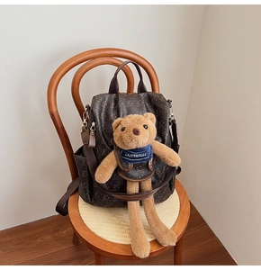 Close-up of a brown floral backpack with a removable blue-scarfed teddy bear plush charm