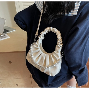 Close-up of white pleated cloud bag featuring glossy pearl chain and textured leather