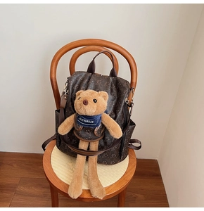Detail of a brown leather backpack with bear prints and a 3D teddy bear plush charm