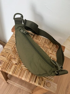 Sac croissant en nylon vert olive sur chaise en rotin avec large bandoulière réglable