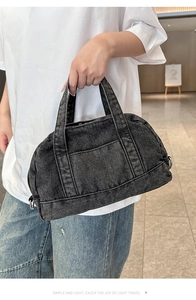 Detail of black denim handbag featuring dual handles and metallic D-rings for straps