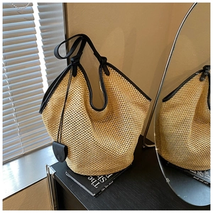 Détail d'un grand sac cabas en paille tissée avec garniture en cuir noir et breloque