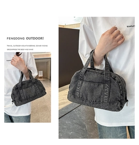Detail of black denim Boston bag featuring double zippers and a front utility pocket