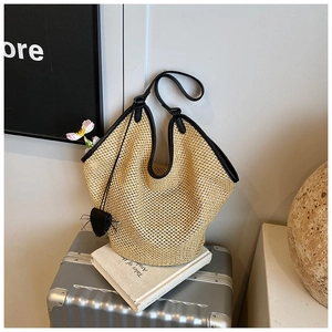 Détail du sac cabas en paille tissée avec anses en cuir noir et breloque en cœur
